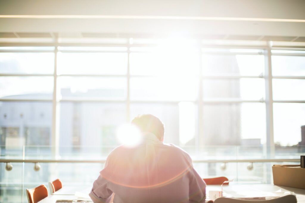 Man working in a building at a desk with the sun shining brightly through the window hes facing